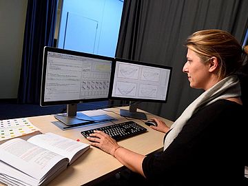 A woman is sitting in front of two PC screens.