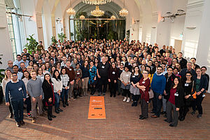 all participants are standing in one group facing the camera, on the floor is a micrope conference banner with the logo
