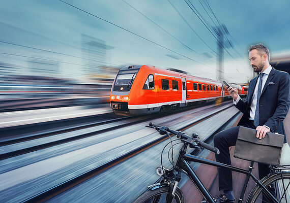 A person with a bicycle is standing at the track and a train passes