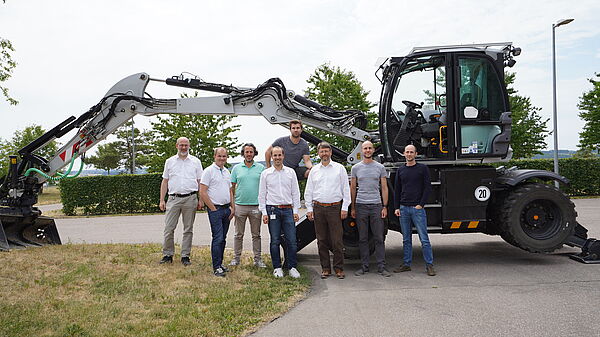 Experts from Bosch and the AIT standing in front of a big excavator