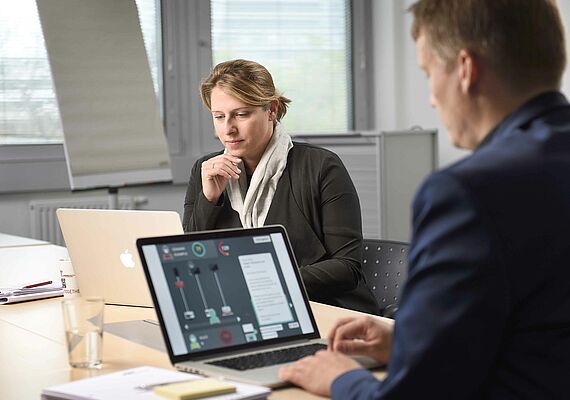 Mann spielt Phishing-Spiel am Laptop. Frau sitzt im Hintergrund.