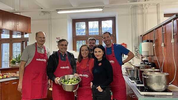 four men and two women standing in the kitchen of Volkshilfe Vienna wearing red aprons