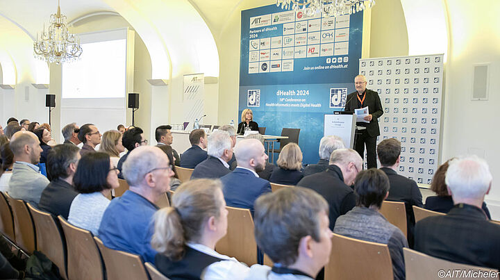 Großer Saal mit Rednerpult, großem dHealth Partnerplakat und 