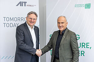 Zwei Personen schütteln sich die Hände vor AIT und JOANNEUM RESEARCH Roll-ups