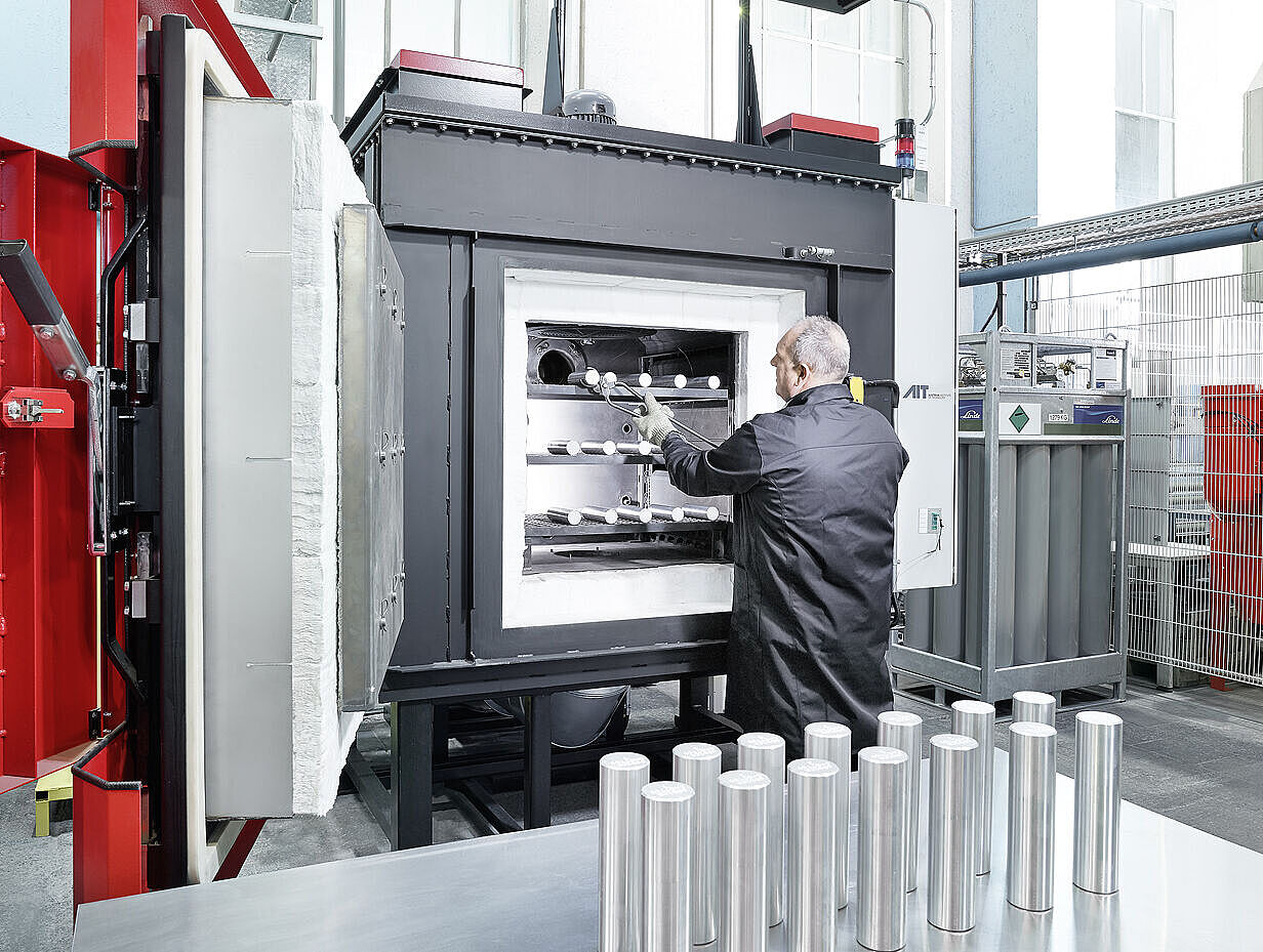 Person stellt Metallproben in geöffneten Wärmeofen