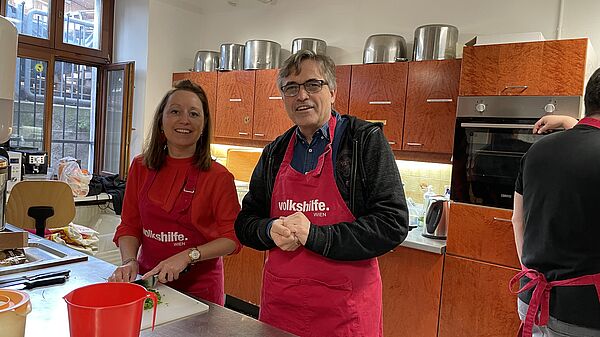 Andreas Vrabl and Angelika Hölbling are smiling into the camera whilst cooking 