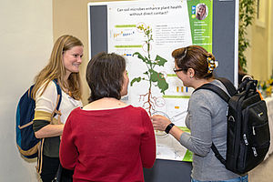 three persons in front of a scientific poster wie plant shematics on it