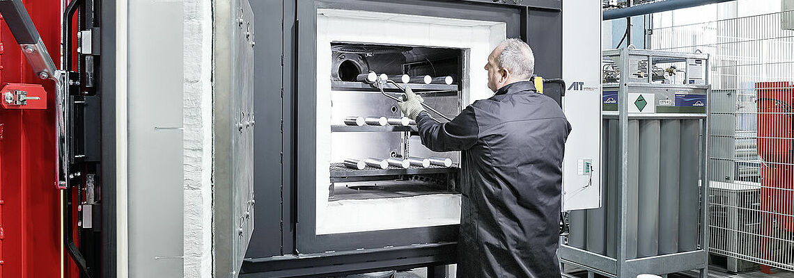 Person stellt Metallproben in geöffneten Wärmeofen