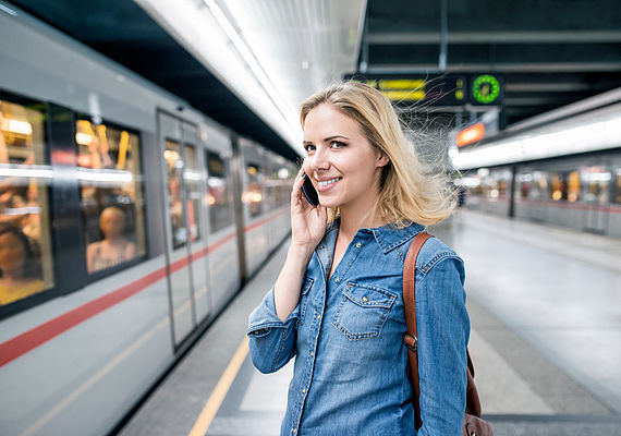 Frau telefonierend bei einer U-Bahnstation während die U-Bahn einfährt