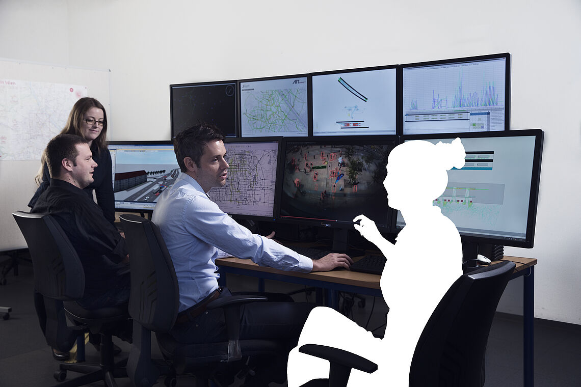 Personen und geweißte Person sitzen vor Computerbildschirmen und besprechen sich