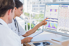 Ärztin sitzt mit Arzt vor einem Monitor und deutet die Auswertung eines EEG im Programm encevis.