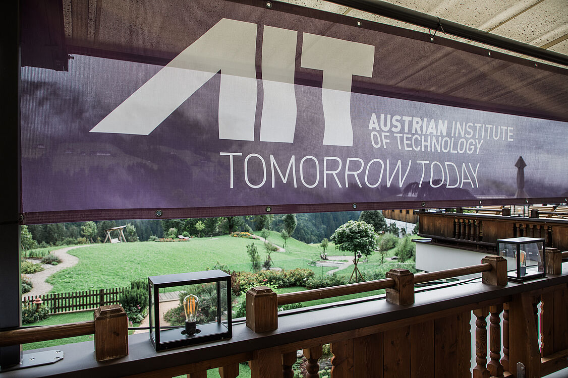 [Translate to English:] Ein Banner mit AIT-Aufschrift, ein Garten im Hintergrund