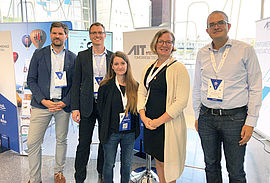 The group of AIT experts standing in front of the AIT booth.