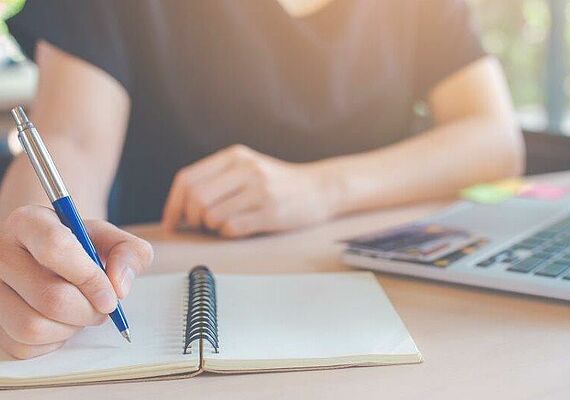 Person writes in a notebook. Only arms are visible.