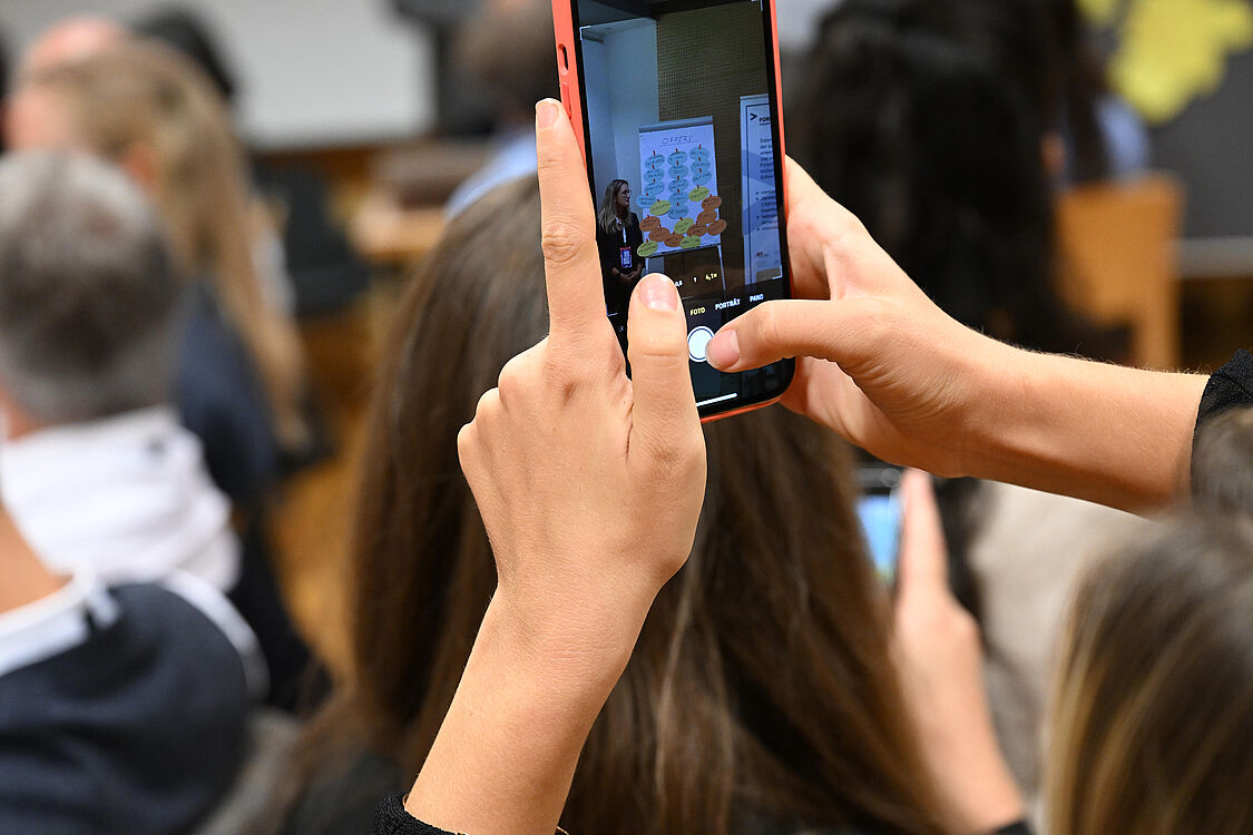 Zwei Hände Fotografieren eine Pinwand mit einem Smartphone