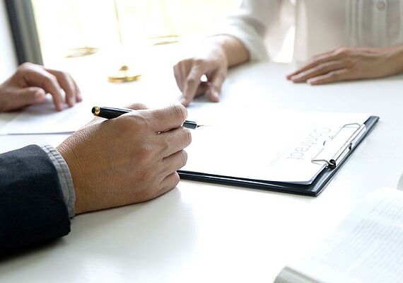 Clipboard is on the table. There are two hands to be seen.