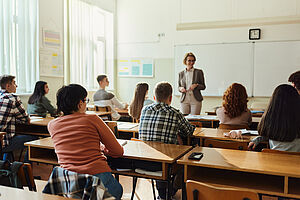 Klassenzimmer von hinten, vorne präsentiert eine Lehrerin