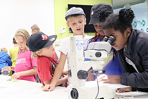 Children look through a microscope and talk to each other