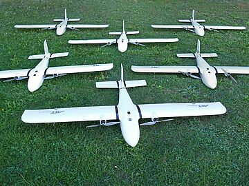 Several unmanned aerial vehicles equipped with sensors and the AIT logo lie on the meadow in front of the AIT Aerial Systems Lab