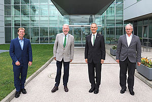 Four men in suits stand slightly apart in front of a building
