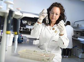 AIT Expertin Eva Maria Sehr im Labormantel und Schutzbrille in ihrem Labor, sie trägt Laborhandschuhe und arbeitet mit Pflanzen- und Samenproben