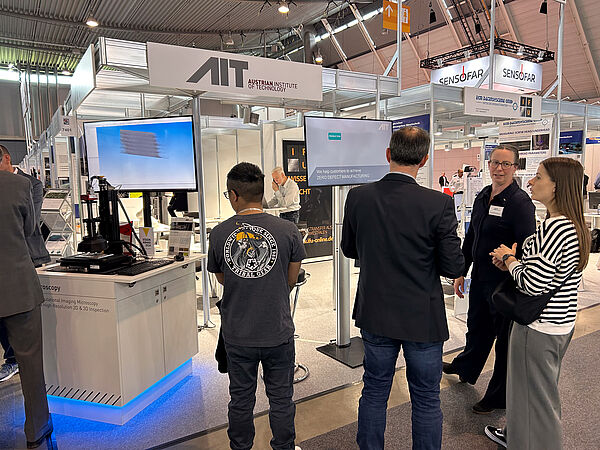 Besucher:innen und AIT Team vor dem AIT Messestand auf der Messe Control