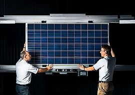 gepulster Sonnensimulator und zwei Forscher halten ein Photovolatik Modul