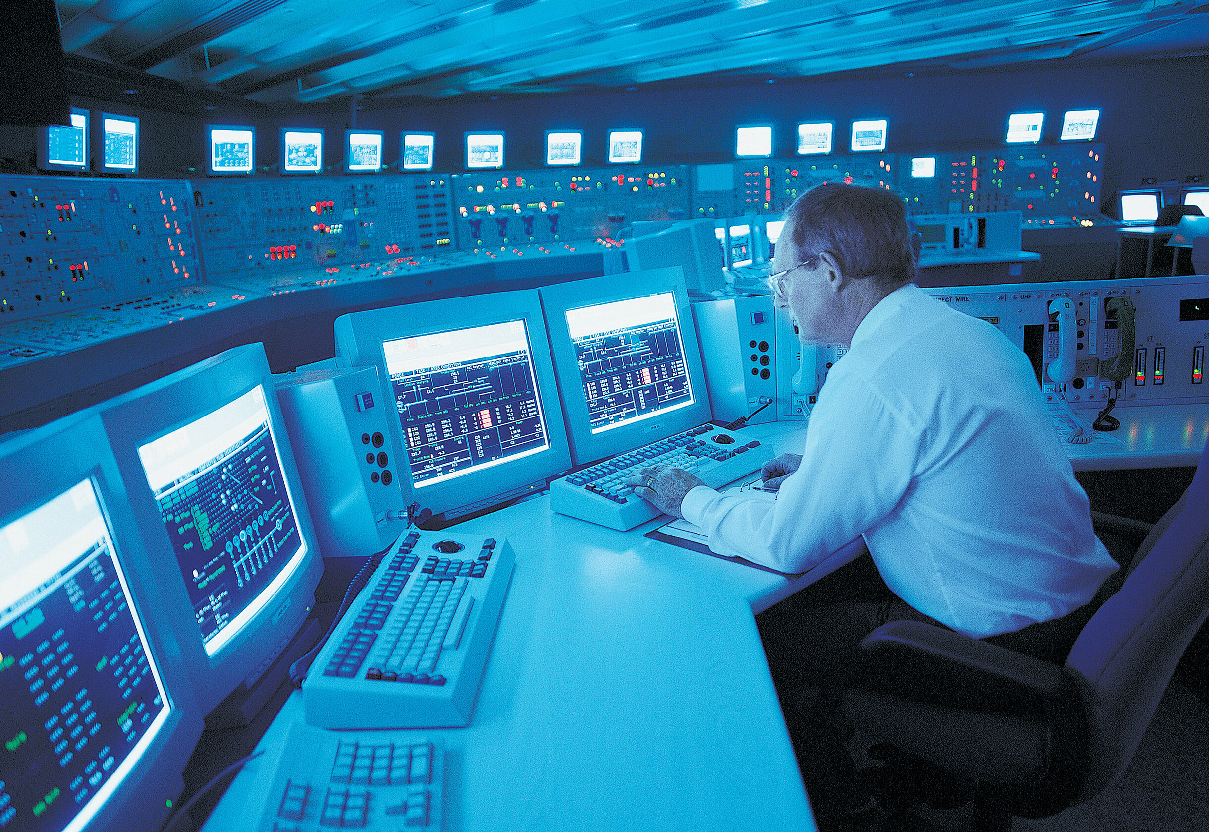 Man sitting at a table with 5 PC screens, in the background many lights