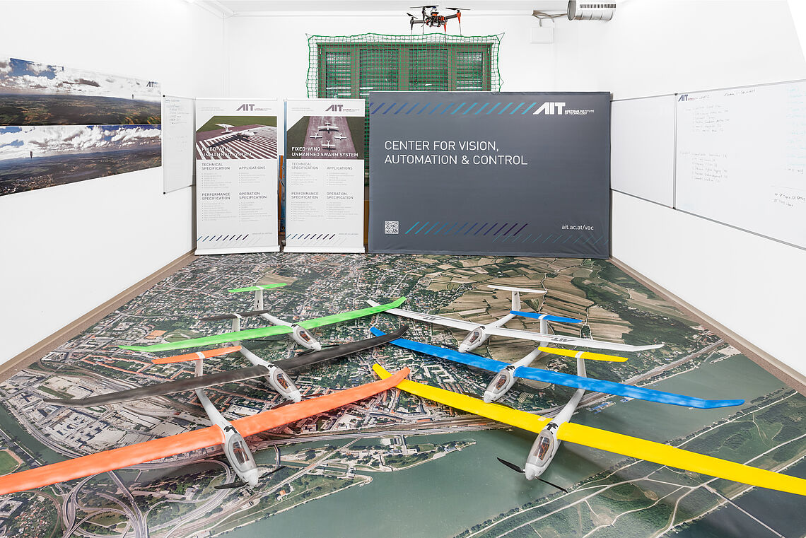 Model airplanes in different colors lie on the ground on a large aerial photograph in the AIT Aerial Systems Lab