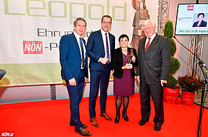 A group of four people stands on the stage, behind them the NÖN Leopold logo, on the right the screen is Angela Sessitsch announced as the winner. On the left side are the two NÖN editors-in-chief, on the right the award-winner Angela Sessitsch and Wolfgang Knoll