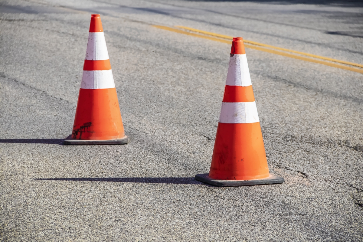 Two grungy orange traffic cones with reflective tape and sharp shadows on cracked asphalt pavement with double yellow line - close-up and selective focus