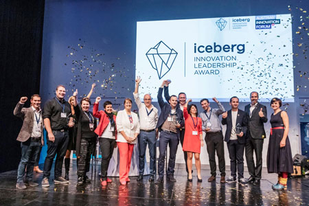 A lot of people from the organisation comitee and the award winner are on stage for a big group photo, in the background is a presentation with the iceberg award logo