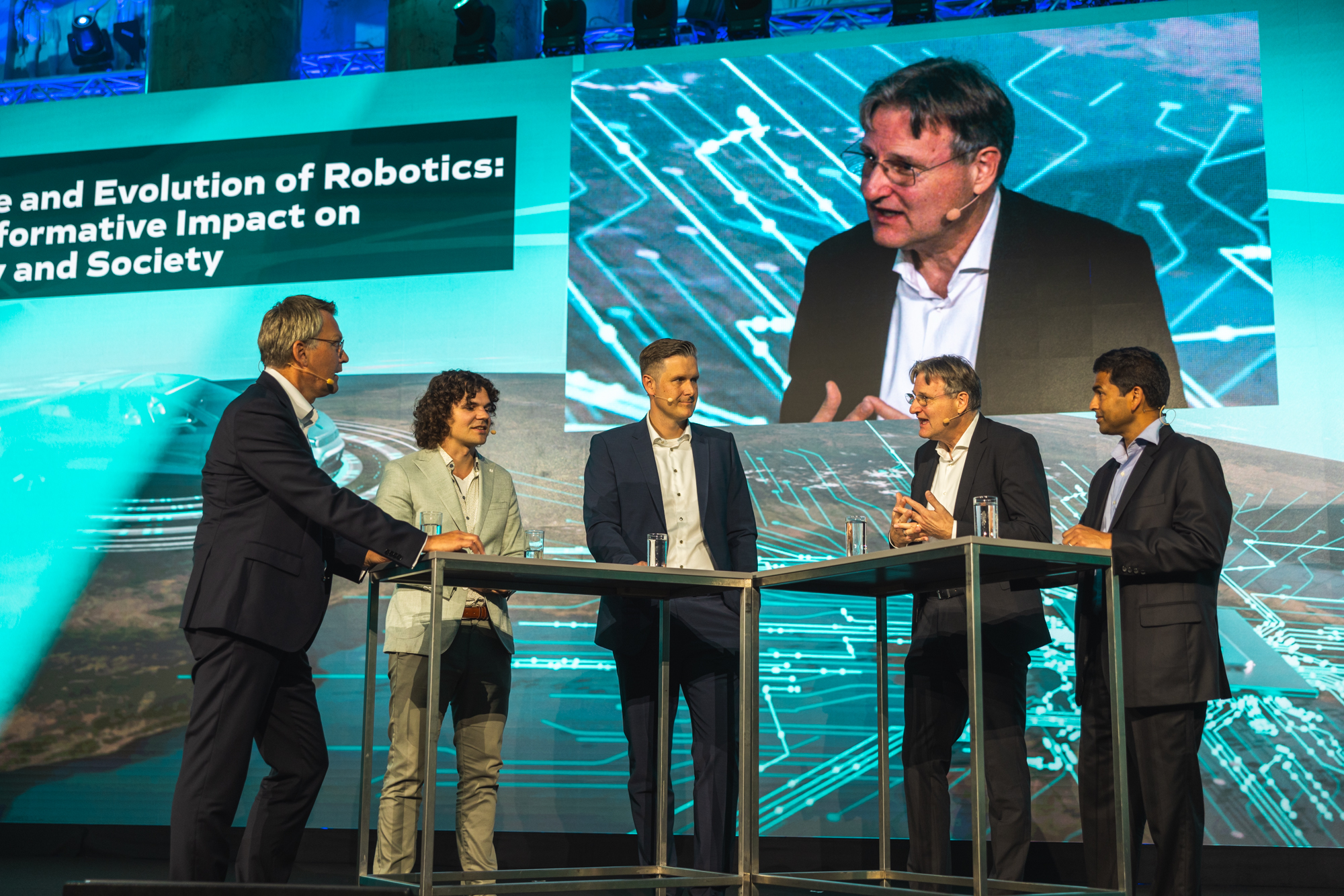 Autonomous Main Event : Experten im Bereich Autonomer Systeme in einer Diskussionsrunde vor blauem Hintergund mit Grafiken, Andreas Kugi groß im Bild. Copyright Christian Steinbrenner